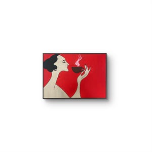 May include: A framed art print featuring a stylized illustration of a woman enjoying a cup of coffee. The artwork has a red background with a black frame. The woman is depicted in profile, with black hair and a neutral skin tone, holding a brown cup with steam rising.