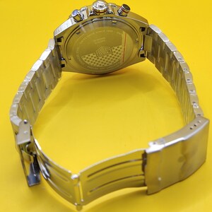 May include: A stainless steel wristwatch with a silver band and a silver watch face. The watch has a round face with multiple dials and buttons. The back of the watch has text that reads "Swiss Made Since 1860".