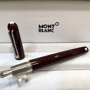 May include: A burgundy Montblanc fountain pen with a silver nib and accents, displayed in an open white box. The pen's cap is off, revealing the nib. The Montblanc logo is visible on the box.
