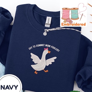 以下が含まれることがあります： 「Off to Commit Mom Foolery」の刺繍とピンクのリボンをつけた漫画のガチョウが特徴のネイビーブルーのスウェットシャツ。スウェットシャツには、白い円の中に「Navy」という文字も入っています。