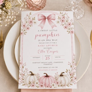 Puede incluir: Una tarjeta de invitación rectangular para baby shower con un lazo rosa, detalles florales y tres calabazas en la parte inferior. El texto dice: A sweet little pumpkin is on her way, please join us for a baby shower honoring Ella Cooper, Saturday August 25 2:00 PM, Harvest Moon Lane, Oakridge, Vermont, RSVP Emma 123-456-789, Registered at Amazon.