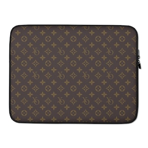 Pode incluir: Uma capa para laptop marrom com um padrão repetido de formas douradas interligadas e as letras "V" e "Q". A capa tem uma borda preta e um fecho de zíper preto.