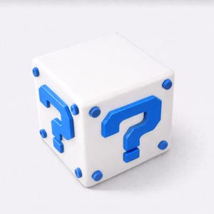 Può includere: Un cubo bianco con punti interrogativi blu su tre lati e dettagli circolari blu. Questo oggetto tridimensionale è probabilmente un oggetto decorativo o un giocattolo.