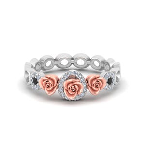 May include: A ring featuring a central rose motif in rose gold surrounded by a halo of small white stones, flanked by two additional rose gold roses and accented with small white stones along the silver band with circular cutouts.