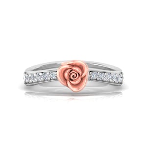 May include: A silver ring featuring a central rose-shaped ornament in rose gold. The band is accented with a row of small, clear, round-cut stones embedded along both sides of the rose, creating a symmetrical design with a polished metallic finish.