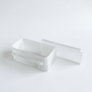 May include: A clear, rectangular container with a matching lid. The container is made of a translucent material, and the lid is slightly ajar. The design is minimalist and modern, suitable for storage.