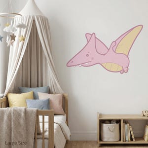Könnte beinhalten: Ein rosa und gelber Cartoon-Pterodaktylus-Wandtattoo. Der Dinosaurier ist im Flug mit ausgebreiteten Flügeln dargestellt. Das Tattoo befindet sich an einer weißen Wand in einem Kinderzimmer. Das Zimmer verfügt über einen Holzbettenrahmen, Kissen und ein Himmelbett.