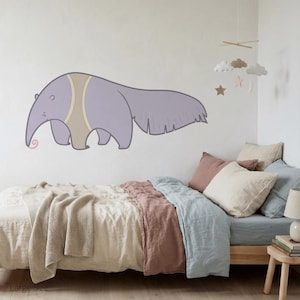Könnte beinhalten: Ein Cartoon-Ameisenbär-Wandtattoo in Lavendel, Beige und Hellrosa wird über einem Bett mit neutralfarbener Bettwäsche gezeigt. Der Raum ist mit einem Mobile mit Wolken, Sternen und einem Mond dekoriert.