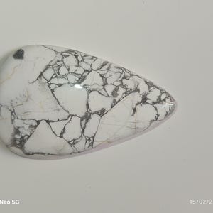 May include: A polished, teardrop-shaped gemstone with a white base and a striking network of black veining. The stone has a smooth, glossy surface and a slightly rounded form, showcasing natural patterns.