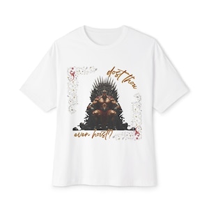 Pode incluir: Camiseta branca com um desenho de uma figura musculosa sentada em um trono de ferro. O texto "dost thou even hoist?" é exibido em uma fonte decorativa, com elementos florais.