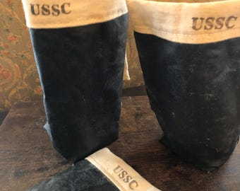 May include: Three black fabric bags with cream-coloured tops and the letters "USSC" printed on them. Two bags are upright, and one is lying flat. The bags appear to be made of a soft, possibly suede-like material.
