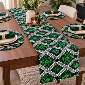 Op de afbeelding: Een tafelloper en bijpassende ronde placemats met een geometrisch patroon in zwart, wit en levendig groen. De set bevat donkergroene stoffen servetten met goudkleurige servetringen, witte borden en goudkleurig bestek op een houten tafel.