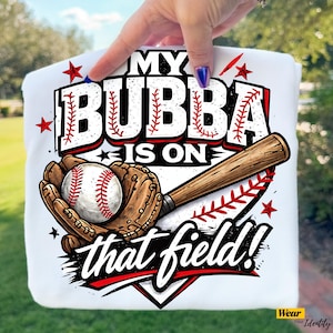 May include: White t-shirt with a baseball-themed graphic. The design includes a baseball, glove, and bat, with the text "MY BUBBA IS ON that field!" in red and black. Red stars and baseball stitching accents complete the design.