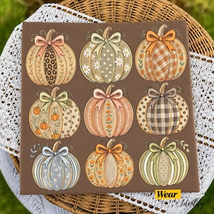 May include: A brown square fabric panel featuring a grid of nine illustrated pumpkins. Each pumpkin displays a unique pattern, including leopard print, gingham, polka dots, and floral motifs, and is topped with a decorative bow in various colors.