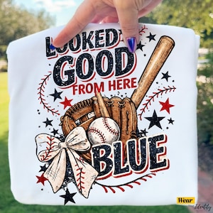 Può includere: Felpa bianca a tema baseball con la scritta "Looked Good From Here" in nero e rosso. Il design include una mazza da baseball, un guanto, una palla e un fiocco. Stelle e cuciture nere e rosse completano il design.