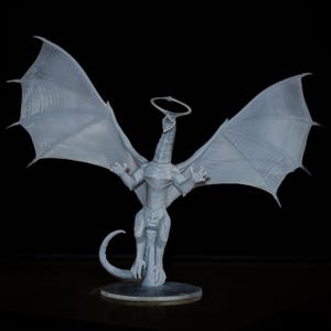 May include: A light gray dragon figurine with outstretched wings and a halo above its head. The dragon is standing on a circular base, with its wings spread wide. The background is black.
