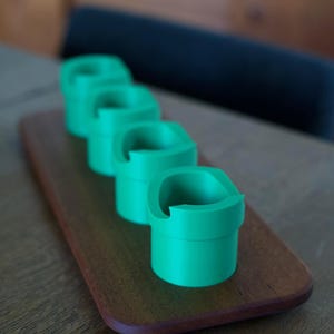 May include: Four bright green cylindrical holders with a distinct notched rim design, arranged in a single row on a rectangular wooden base. Each holder features a smooth, matte finish and a consistent shape, creating a uniform appearance.