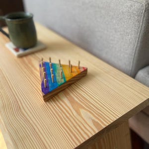 May include: A wooden side table with a natural finish. A colorful, triangular wooden toy with pegs is on the table. A green mug sits on a coaster in the background. The table is next to a gray sofa.