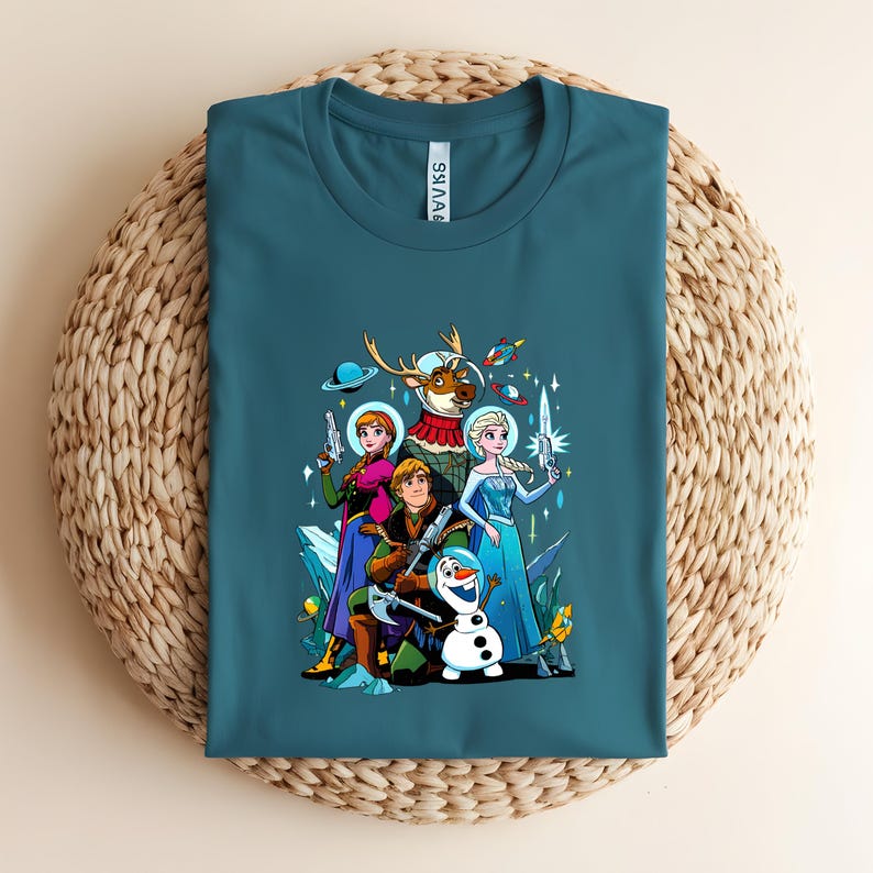 Op de afbeelding: Tealkleurig T-shirt met een kleurrijke afbeelding van geanimeerde personages in ruimte-thema outfits. Het ontwerp bevat een rendier in een ruimtepak, een sneeuwpop en andere personages die futuristische wapens vasthouden.