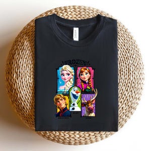 May include: Black t-shirt featuring the word "FROZEN" above a graphic of characters from the movie, including Elsa, Anna, Olaf, Kristoff, and Sven. The shirt is made of a soft material and is suitable for casual wear.