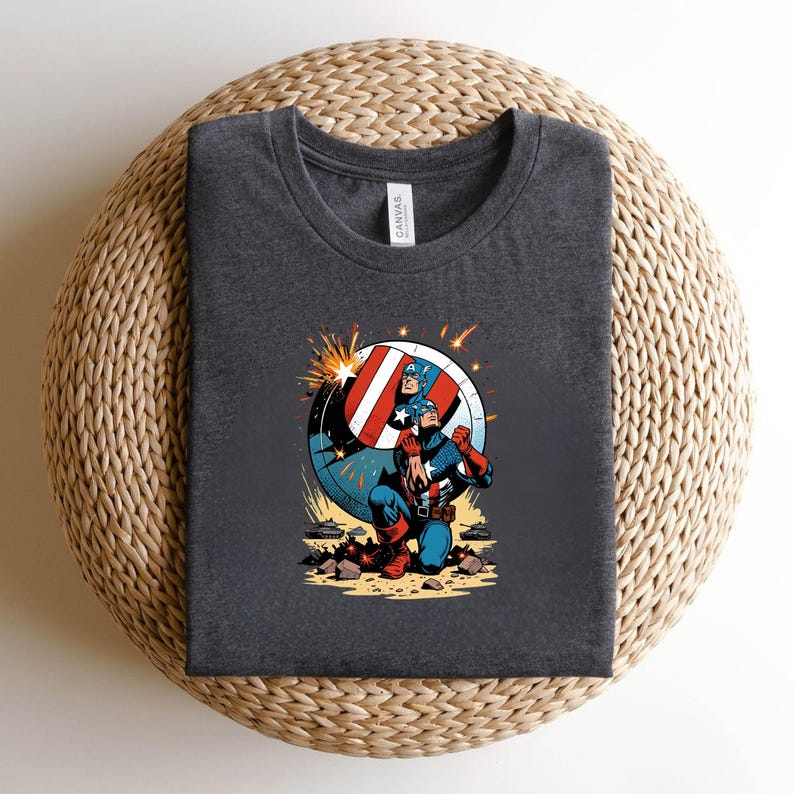 Puede incluir: Camiseta gris oscuro con un dise&ntilde;o de Capit&aacute;n Am&eacute;rica. El dise&ntilde;o muestra al Capit&aacute;n Am&eacute;rica arrodillado con su escudo, en colores rojo, blanco y azul. La camiseta est&aacute; hecha de un material suave.