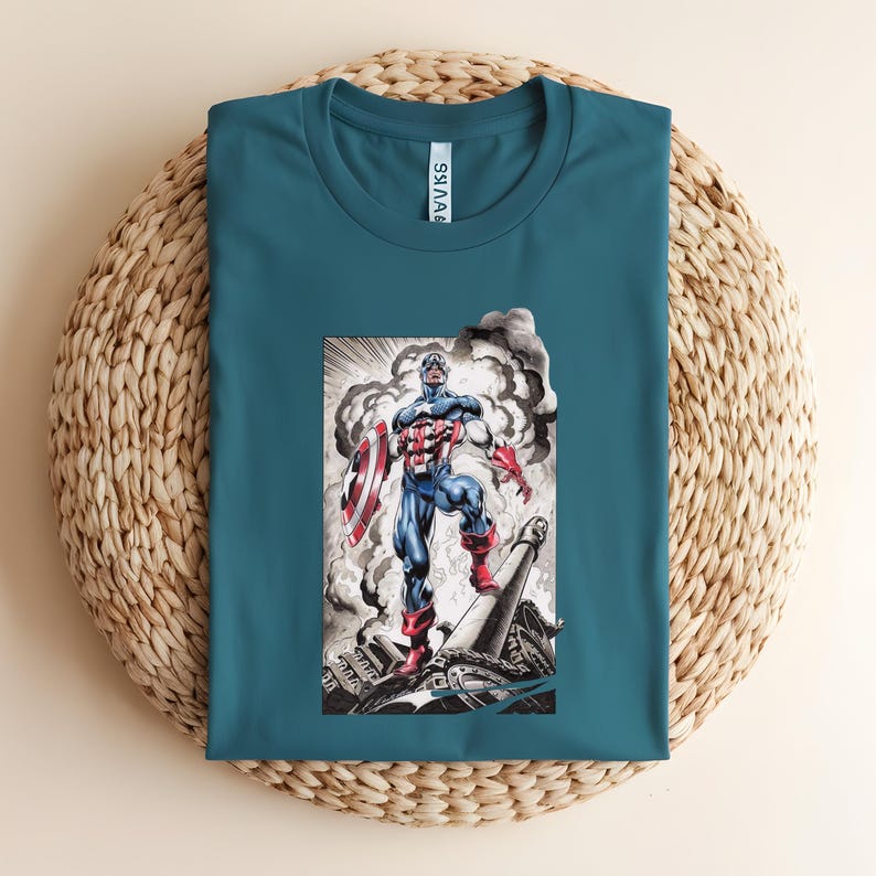 May include: Teal-colored t-shirt featuring a graphic of Captain America in a heroic pose, holding his shield amidst a smoky background. The illustration is detailed with red, white, and blue colors, capturing the iconic superhero's attire. The shirt is folded on a woven surface.