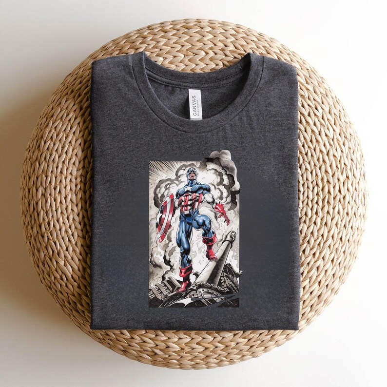 May include: Dark gray t-shirt featuring a graphic of Captain America with his shield, standing amidst a smoky, war-torn scene. The illustration is in shades of red, white, blue, and gray. The shirt is made of a soft material.