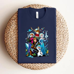Op de afbeelding: Marineblauw T-shirt met een kleurrijke cartoonafbeelding van personages uit de film Frozen, waaronder Elsa, Anna, Kristoff, Olaf en Sven, in een ruimtethema-ontwerp. De afbeelding bevat ruimteschepen, planeten en straalpistolen.