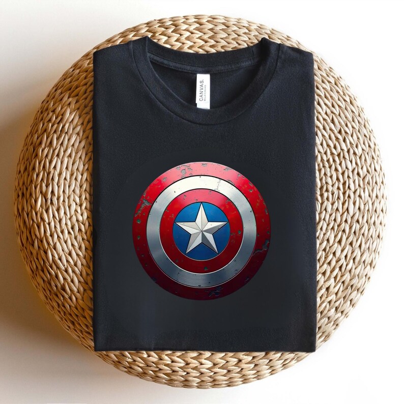 May include: A black crew neck t-shirt featuring a centred graphic of a circular shield with a distressed red, white, and blue finish. The shield design includes a prominent white five-pointed star set against a blue circular background.