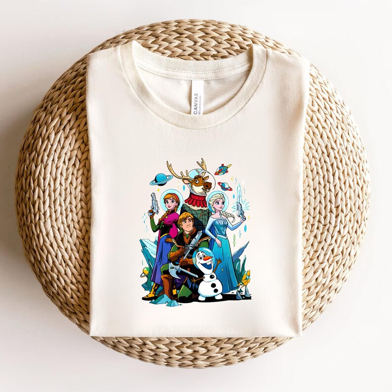 Op de afbeelding: Cr&egrave;mekleurig T-shirt met een kleurrijke cartoonillustratie van personages uit de film Frozen. De afbeelding toont Elsa, Anna, Kristoff, Olaf en Sven, elk met futuristische straalkanonnen en ruimtehelmen.