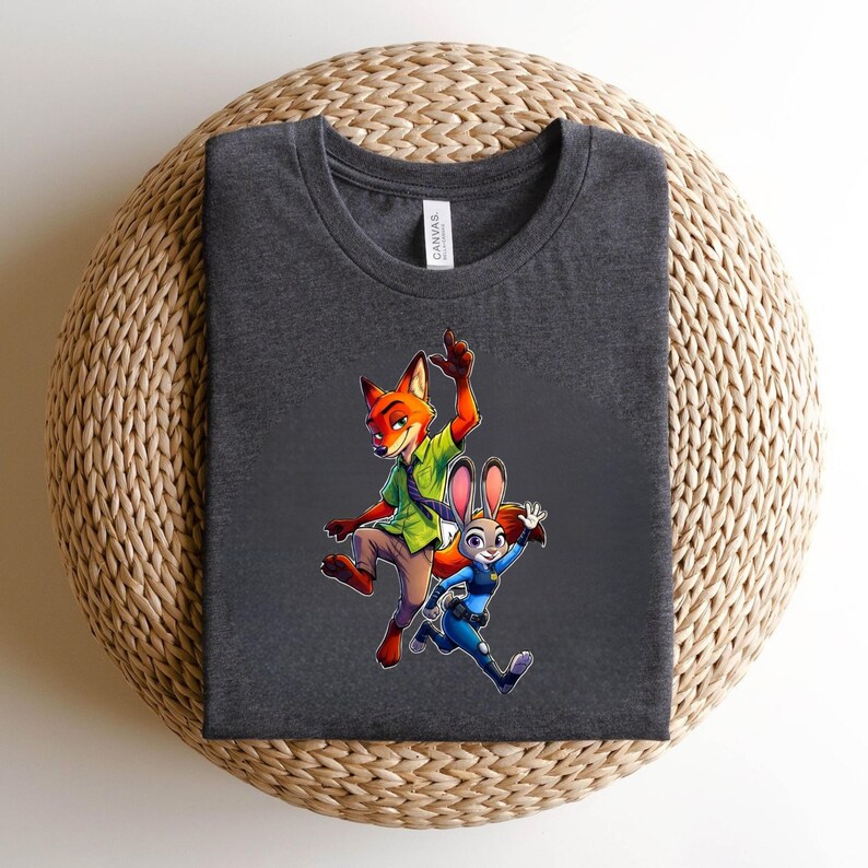 Puede incluir: Una camiseta de cuello redondo gris carb&oacute;n oscuro con un estampado gr&aacute;fico de un zorro de dibujos animados con camisa verde y un conejo de dibujos animados con uniforme de polic&iacute;a azul. El zorro salta con un brazo alzado y el conejo corre.