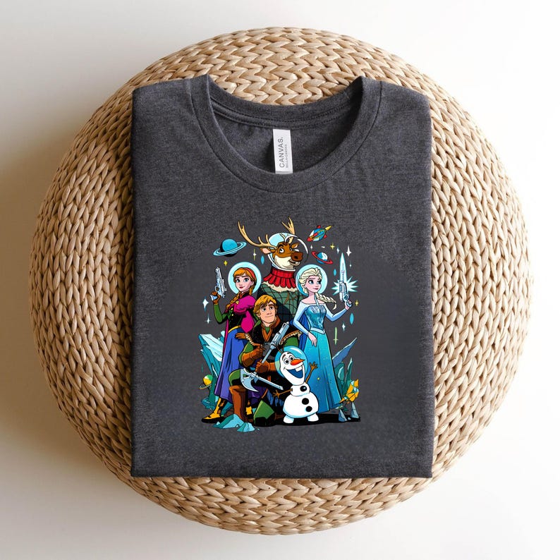 Op de afbeelding: Donkergrijs t-shirt met een kleurrijke afbeelding van stripfiguren in een ruimtethema-ontwerp. De afbeelding bevat personages met wapens en ruimte-elementen. Het shirt wordt weergegeven op een geweven oppervlak.