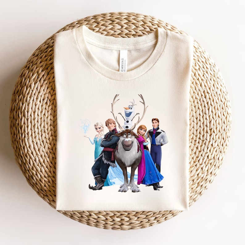 Op de afbeelding: Cr&egrave;mekleurig T-shirt met een afbeelding van personages uit de animatiefilm "Frozen". Het ontwerp omvat Elsa, Anna, Kristoff, Sven, Olaf en Hans. Het shirt heeft een ronde hals en is gemaakt van een zacht materiaal.