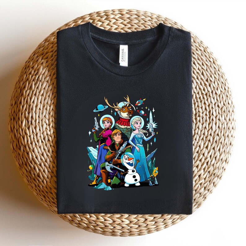Op de afbeelding: Zwart T-shirt met een kleurrijke afbeelding van personages uit de film Frozen, waaronder Elsa, Anna, Kristoff, Olaf en Sven, in een ruimtethema-ontwerp. Het ontwerp bevat straalpistolen, planeten en ruimtehelmen. Het shirt wordt getoond op een geweven oppervlak.