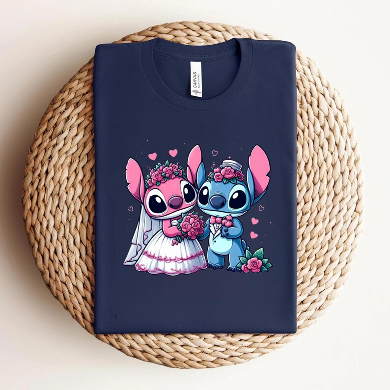 May include: A navy blue t-shirt featuring a graphic of two cartoon characters dressed for a wedding. One character is pink with a white veil and a bouquet of pink roses, while the other is blue with a bow tie and a top hat, surrounded by hearts.