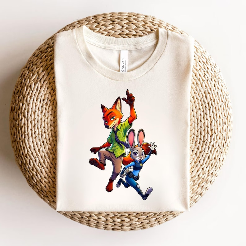 Puede incluir: Una camiseta de color crema con un estampado gr&aacute;fico de un zorro rojo con camisa verde y corbata morada, y un conejo gris con uniforme azul. El zorro salta con un brazo levantado, mientras que el conejo corre con un brazo levantado.