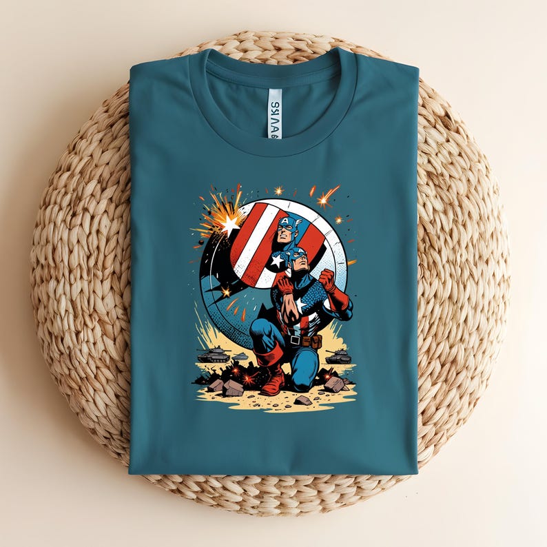Puede incluir: Camiseta verde azulado con un gr&aacute;fico del Capit&aacute;n Am&eacute;rica. El dise&ntilde;o muestra al Capit&aacute;n Am&eacute;rica arrodillado, con su escudo. La ilustraci&oacute;n utiliza colores vibrantes y l&iacute;neas de acci&oacute;n, sobre un fondo de escudo circular.