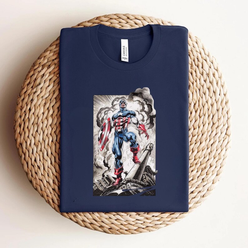 May include: Navy blue t-shirt featuring a graphic of Captain America in a heroic pose, holding his shield. The illustration is in a comic book style with a background of smoke and debris. The shirt is folded on a woven surface.