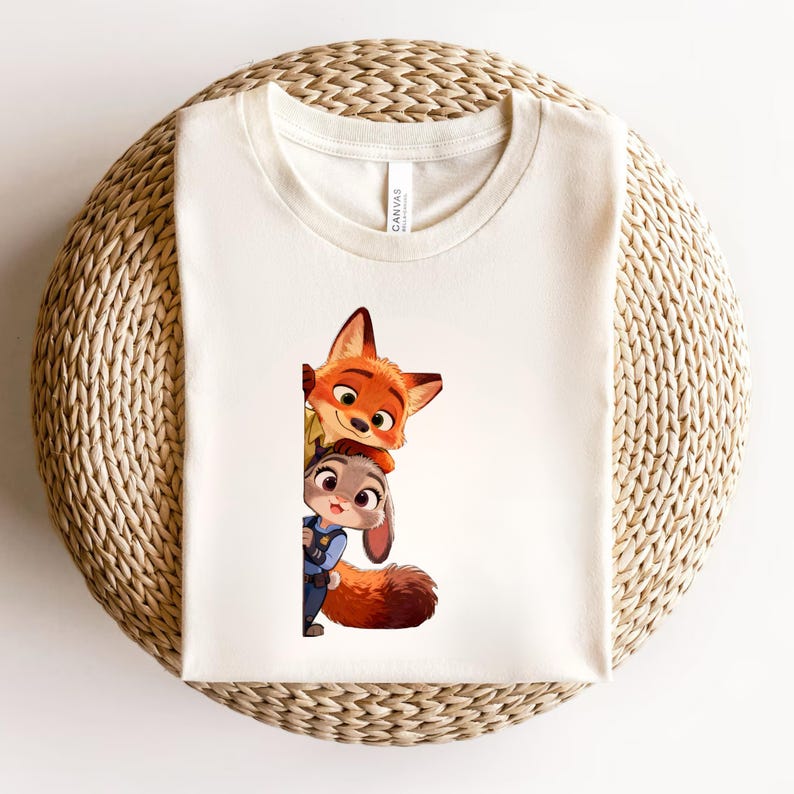 May include: A cream-colored t-shirt featuring a graphic print of a cartoon fox and a cartoon rabbit peeking out from behind a vertical edge. The fox has orange fur and large ears, while the rabbit wears a blue uniform with a badge.