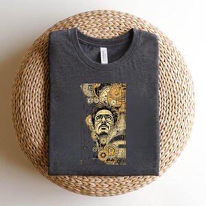 Pode incluir: Camiseta cinza escuro com um gr&aacute;fico detalhado de um homem com &oacute;culos, em um fundo de engrenagens douradas e elementos de relojoaria. O design &eacute; em estilo retrato, com uma est&eacute;tica vintage e steampunk.
