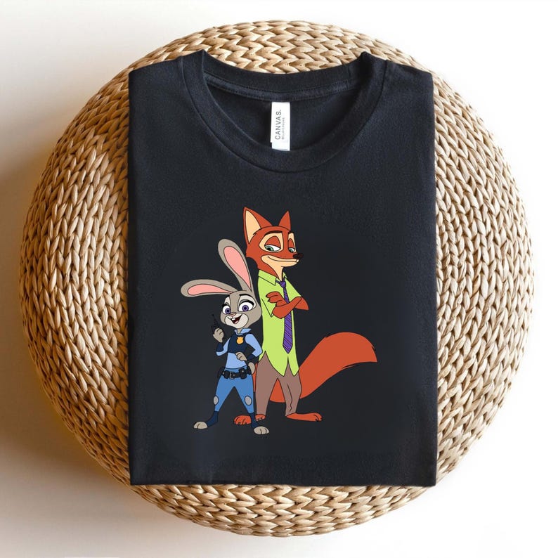Peut inclure: Un t-shirt noir avec une impression graphique repr&eacute;sentant un lapin de dessin anim&eacute; en uniforme de police bleu et un renard de dessin anim&eacute; en chemise verte et cravate violette. L'&eacute;tiquette blanche au col porte le nom de marque Canvas.