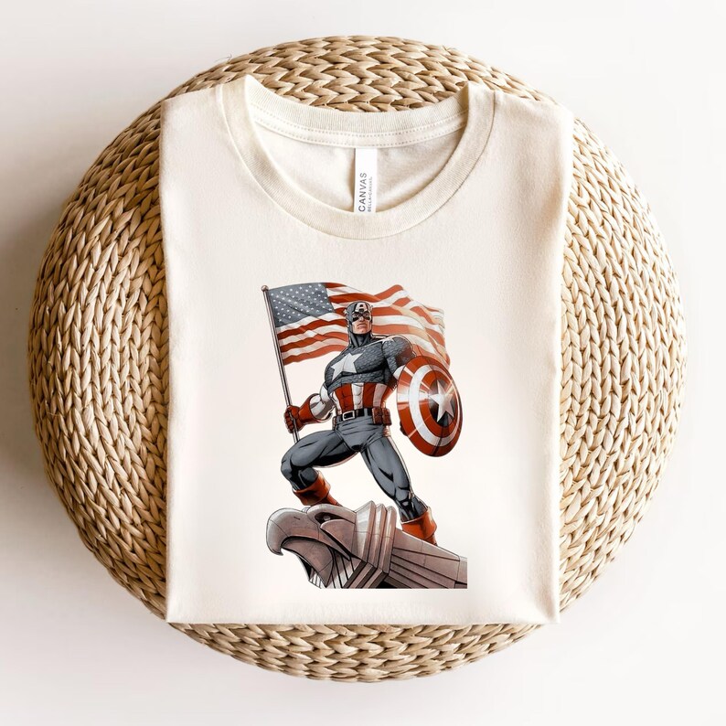 Pode incluir: Camiseta creme com um gr&aacute;fico do Capit&atilde;o Am&eacute;rica segurando uma bandeira e um escudo americanos. O super-her&oacute;i &eacute; retratado em uma pose din&acirc;mica, com a bandeira tremulando atr&aacute;s dele. A camisa &eacute; feita de um material macio.