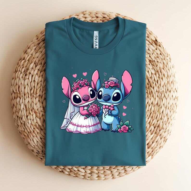 May include: A teal crew neck t-shirt featuring a graphic of two cartoon characters dressed for a wedding. One character is pink with a white veil and flower crown, holding a bouquet. The other is blue with a top hat and bowtie, both with pink hearts.