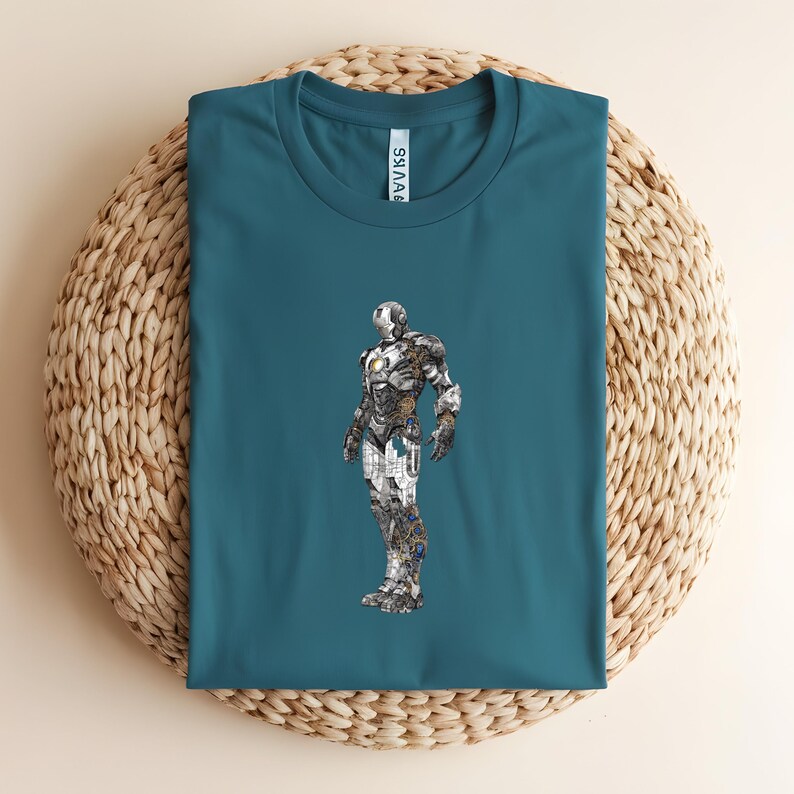 May include: Teal-colored t-shirt featuring a detailed illustration of a metallic superhero. The superhero design incorporates silver, gray, and gold tones, creating a striking contrast against the shirt's background. The shirt is laid on a woven, beige surface.