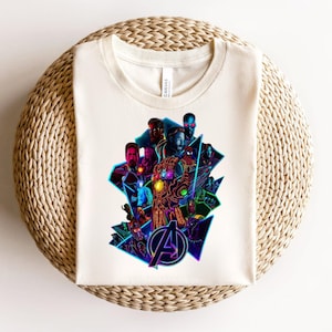 May include: Off-white t-shirt with a colourful graphic of various superheroes, including Iron Man and Captain America, and the Avengers logo. The design incorporates neon blue and purple highlights.