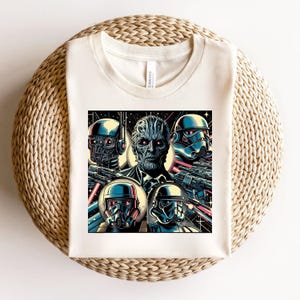 May include: Off-white t-shirt featuring a colorful graphic of four characters with helmets and weapons. The central figure has a textured face and red eyes. The design includes blue, black, and red accents, with a space-themed background.