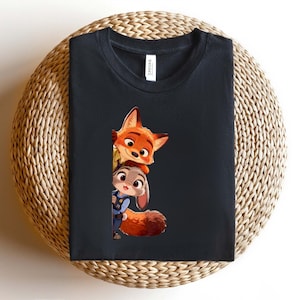 May include: A black crew neck t-shirt featuring a graphic print of a cartoon fox and a cartoon rabbit peeking out from the side. The fox is orange with large ears, and the rabbit is gray with a blue uniform, both rendered in a colorful style.