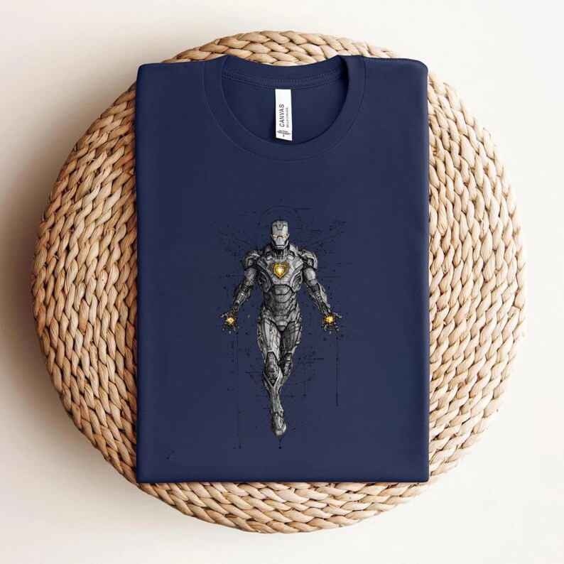 Op de afbeelding: Marineblauw t-shirt met een gedetailleerde illustratie van Iron Man. Het ontwerp toont het pantser van het personage met een gloeiende boogreactor. Het shirt is op een geweven oppervlak gevouwen.
