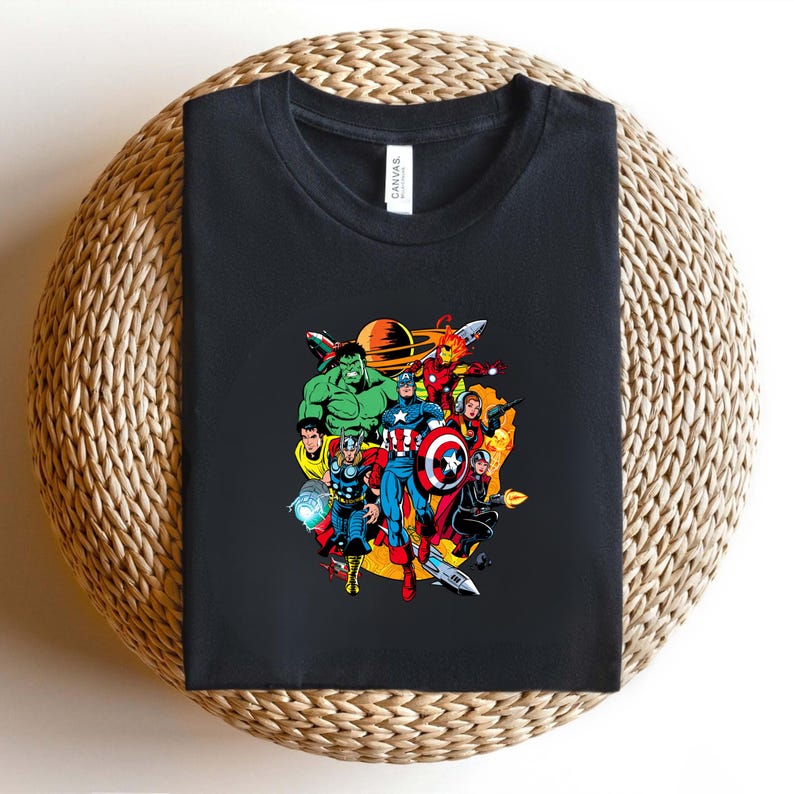 May include: A black crew neck t-shirt featuring a colorful graphic print of various comic book superheroes in a space setting with a planet in the background. The shirt has a white tag at the inner neckline with the brand name Canvas printed on it.