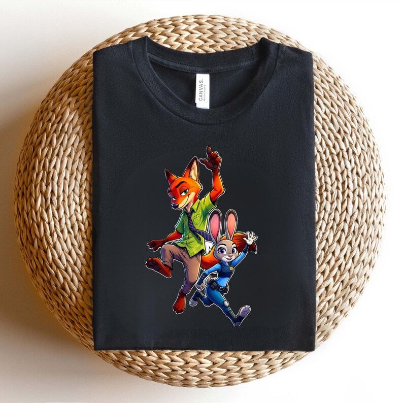 Puede incluir: Una camiseta negra con un estampado gr&aacute;fico de un zorro de dibujos animados con camisa verde y pantalones marrones, y un conejo de dibujos animados con uniforme de polic&iacute;a azul. Los personajes aparecen en una pose din&aacute;mica de carrera.